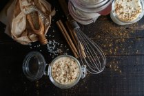 Стеклянные банки сладкого десерта риса с молоком и корицей на деревянном столе с ингредиентами — стоковое фото