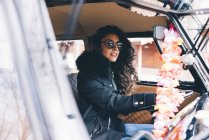 Young woman in black coat and sunglasses sitting inside car — Stock Photo