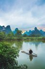 Chinese man sitting on raft on river with picturesque mountains on background, Guangxi, China — Stock Photo