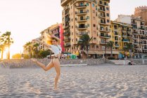 Femme gaie dansant sur une jambe sur la plage au coucher du soleil — Photo de stock