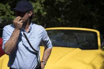 Человек, говорящий по радио снаружи перед современной желтой машиной — стоковое фото