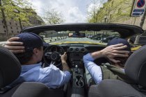 Visão traseira de dois homens que dirigem no carro rápido moderno para baixo da estrada da cidade na luz solar — Fotografia de Stock