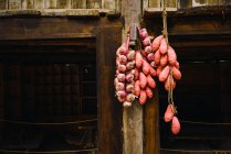 Chinese sweet potatoes and garlic hanging in bunches on wooden wall — Stock Photo