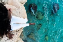 Frau sitzt auf Klippe über kristallklarem türkisfarbenem Wasser — Stockfoto