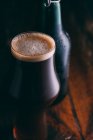 Толстое пиво в стекле и бутылка на темном деревянном фоне — стоковое фото
