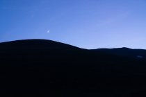 Paesaggio minimalista di silhouette nera delle colline montane contro il cielo blu crepuscolo con luna crescente — Foto stock