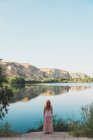 Woman in long summer dress standing on lake shore — Stock Photo