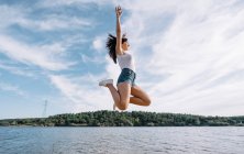 Весела жінка стрибає біля озера . — стокове фото