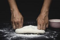 Human hands kneading dough on tabletop on black background — Stock Photo