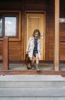 Blondes Mädchen im Trenchcoat mit lederner Aktentasche läuft vor Holzhaus — Stockfoto