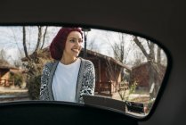 Junge Frau mit Wollmütze steht im Grünen hinter Auto — Stockfoto