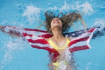 Расслабленная улыбающаяся женщина, плескающаяся в бассейне с американским флагом — стоковое фото