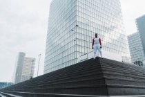Человек в спортивной одежде стоит на лестнице с современными стеклянными небоскребами на заднем плане — стоковое фото