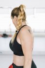 Blondine in Sportbekleidung steht auf verschwommenem Hintergrund des Fitnessstudios und schaut weg — Stockfoto