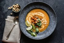 Thai-Kürbissuppe mit Limetten und Erdnüssen in grauem Teller auf grauer Oberfläche — Stockfoto