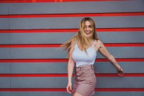 Junge Frau in lässigem Outfit lacht, während sie an gestreifter Wand steht — Stockfoto