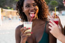 Mujeres juguetonas disfrutando de bebidas en la playa - foto de stock