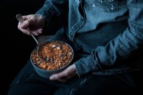 Mains masculines tenant un bol de granola de quinoa croquant sur fond sombre — Photo de stock