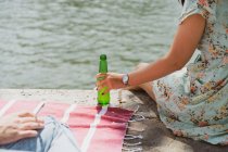Weibliche Hand hält Flasche Bier am Wasser — Stockfoto