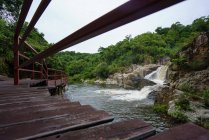 View of small waterfall among rocks in Yanoda Rainforest with wooden walkway on side, China — Stock Photo