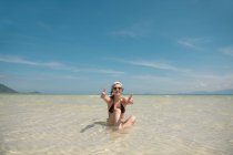 Femme joyeuse geste pouces levés et assis dans l'eau de l'océan — Photo de stock