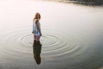 Young woman standing in clear water of lake and looking over shoulder in daylight — Stock Photo