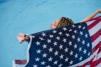 Sorrindo mulher dentro segurando bandeira americana na piscina — Fotografia de Stock