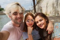 Усміхаючись молоді жінки і чоловік у повсякденний одяг, беручи selfie на відкритому повітрі — стокове фото