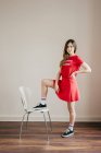 Девушка в красном наряде позирует с одной ногой на стуле — стоковое фото