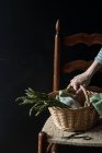 Human hand holding basket of fresh green asparagus on chair on black background — Stock Photo
