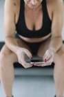 Athlète féminine assise sur un banc et utilisant une application de fitness sur smartphone — Photo de stock