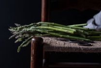 Gros plan de bouquet d'asperges vertes fraîches sur chaise sur fond noir — Photo de stock