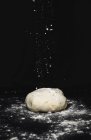 Powdering dough with flour on kitchen tabletop on black background — Stock Photo