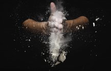 Mani umane scuotendo farina e pezzi di pasta su sfondo nero — Foto stock