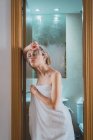 Очаровательная молодая женщина, завернутая в белое полотенце, стоящая в дверях ванной комнаты — стоковое фото
