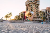Mujer joven flexible saltando en la playa con edificios en el fondo - foto de stock