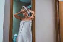 Young woman standing in bathroom doorway and using towel to dry hair after shower at home — Stock Photo