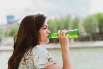 Junge Frau im Sommerkleid trinkt Wasser am Wasser — Stockfoto