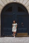 Femme en robe d'été à motifs avec imprimé floral s'appuyant sur la porte minable et détournant les yeux — Photo de stock