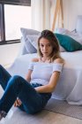 Thoughtful young woman sitting on floor near sofa — Stock Photo