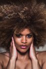 Close-up de mulher étnica com cabelo afro tocando rosto e olhando sensualmente para a câmera — Fotografia de Stock