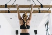 Back view of strong woman in sportswear hanging on wooden board in gym and pulling up — Stock Photo