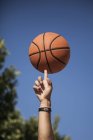 Мужская рука вращающийся баскетбол на пальце с голубым небом на фоне — стоковое фото