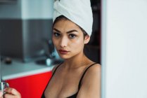 Junge Frau mit Handtuch auf dem Kopf schaut zu Hause in die Kamera — Stockfoto