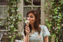 Young woman holding ice-cream in front of window with creeping plant — Stock Photo
