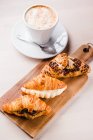 Assorted croissants with filling on wooden board and cup of cappuccino — Stock Photo