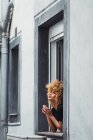 Кучерява етнічна жінка дивиться з вікна — стокове фото