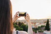 Mulher tirando foto da cidade ao pôr do sol — Fotografia de Stock