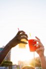 Mani femminili clinking con tazze di plastica di bevande in luce solare brillante sulla strada — Foto stock