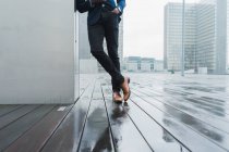 Beine eines Geschäftsmannes lehnen bei Regen im Freien an Wand — Stockfoto